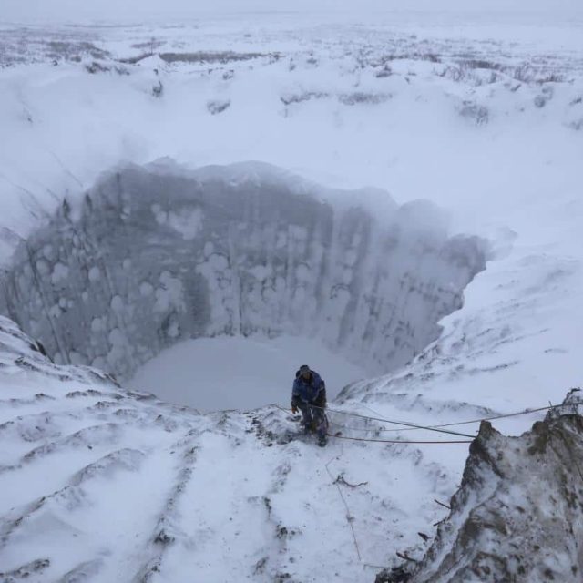 Cratère glacé enneigé avec explorateur descendu en rappel dans la blancheur polaire