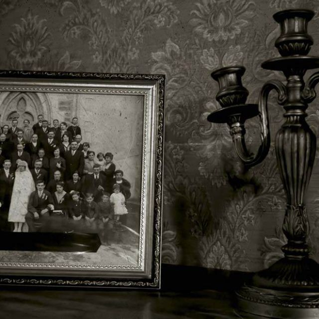 Cadre avec portrait de groupe en noir et blanc et chandelier sur papier peint sombre, salle Le manoir des sœurs Aubépine à Angers