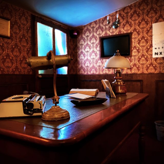 Bureau rétro aux murs damassés, téléphone et lampe vintage sur le bureau d'Échappe Toi Si Tu Peux