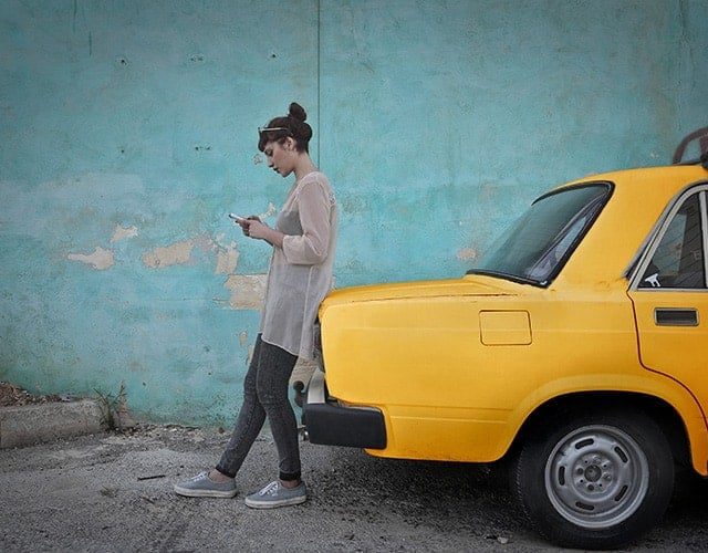 Femme face à un taxi jaune rétro devant un mur turquoise délabré