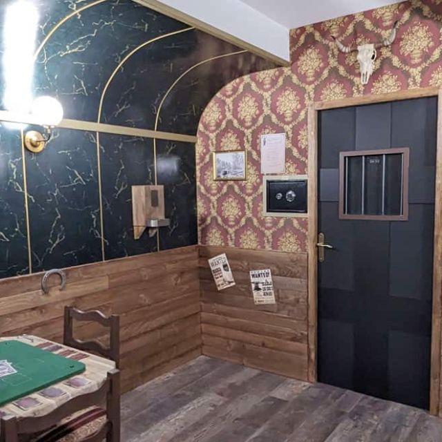 Wagon aux murs de faux marbre vert, table de jeu verte et porte de cellule, salle Le Silver Express à Angers