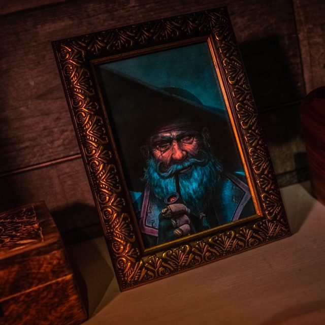 Cadre doré avec portrait d'un homme barbu à l'expression sombre, décor pirate de la salle Le navire maudit