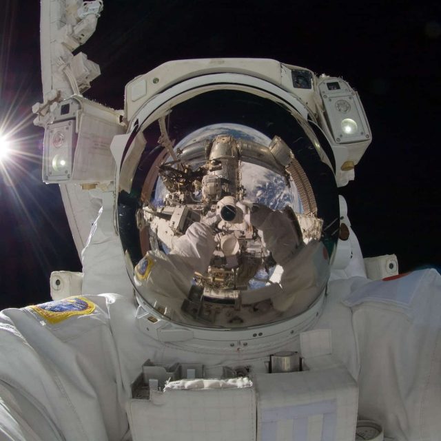 Astronaute en combinaison spatiale dans l'espace, casque réfléchissant la Terre, chez Spatial Xcape