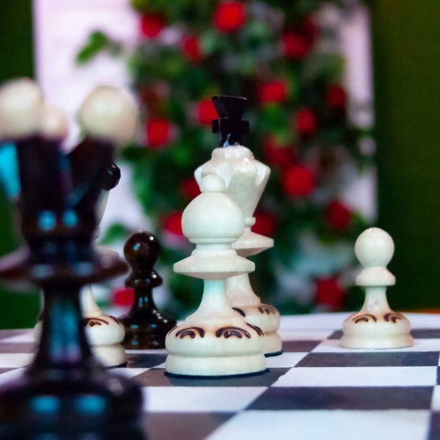 Pièces d'échecs blanches et noires sur un échiquier, rosier en fond, salle Au pays des merveilles chez Locked Time