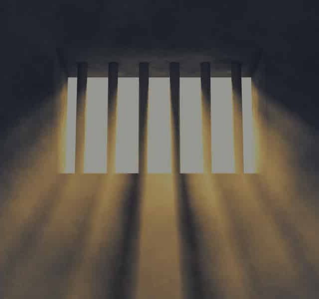Cellule de prison avec barreaux, lumière crue passant par étroite fenêtre dans la salle Tel Est Pris Qui Croyait Prendre
