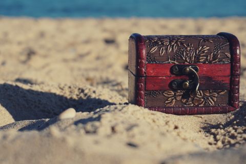 Vieux coffre pirate entreouvert sur plage de sable sous ciel bleu