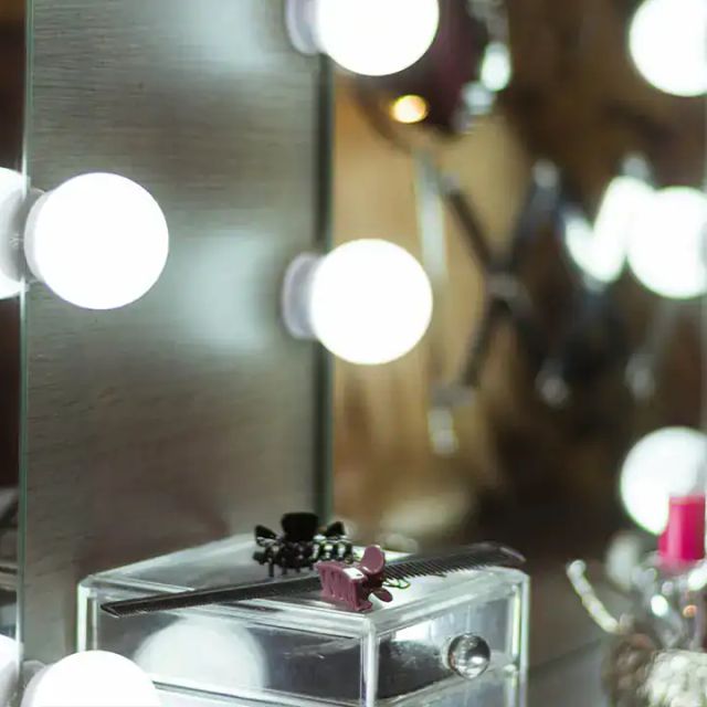 Miroir de loge entouré d'ampoules et flacons de maquillage, salle Enquête Burlesque