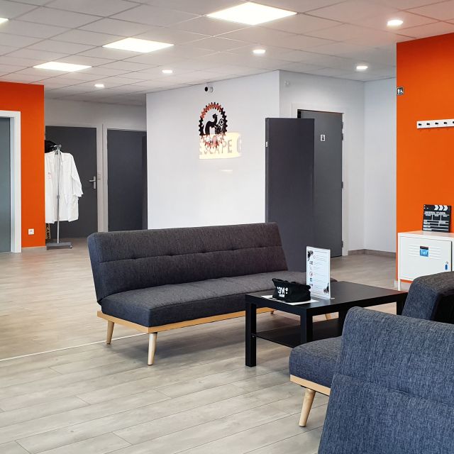 Accueil du Weasel Escape Game avec murs orange, canapés gris et portes noires
