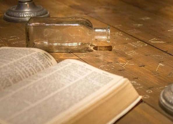 Livre ouvert et bouteille vide sur table en bois usée, décor d'enquête au château