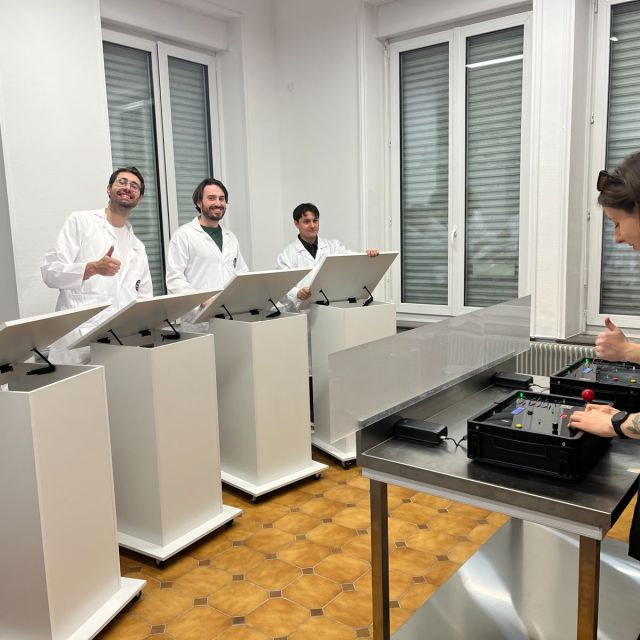 Joueurs en blouse blanche derrière des pupitres dans un laboratoire, Stop The Bomb