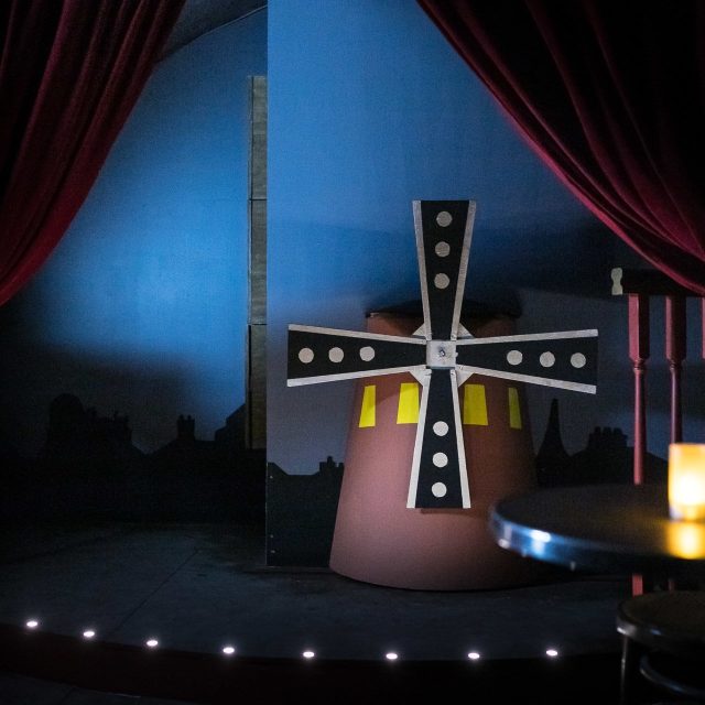 Décor de moulin avec croix illuminée, rideaux rouges et ambiance nocturne chez Prizoners à Paris
