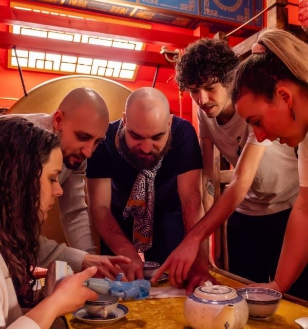 Groupe de joueurs penchés autour d'un service à thé sur une table jaune, décor rouge, salle La cité interdite à Strasbourg