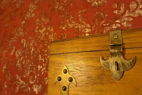 Coffre en bois à fermoirs dorés devant un mur rouge à motifs, salle Les souterrains de Richelieu chez La Boîte à CL-é