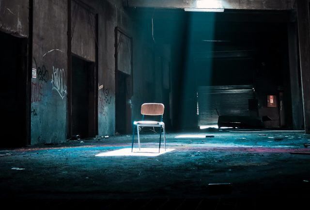 Chaise seule éclairée par un faisceau bleu dans une grande salle sombre, salle Sacrifice à Les Pennes-Mirabeau
