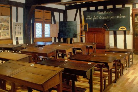Salle de classe ancienne aux pupitres de bois alignés et tableau noir, salle L'examen final chez The Clock à Rodez