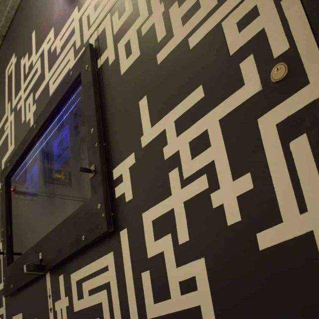 Paroi de labyrinthe noir et blanc avec écran encastré, décor de la salle Police Academy chez Happy Hour Escape Game à Paris