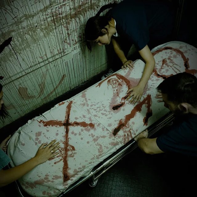 Trois joueurs examinent un corps sur une table dans une ambiance d'hôpital sinistre chez Freeing!