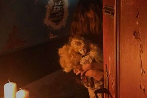 Poupée aux cheveux bouclés et bougies près d'une porte de bois sombre, salle L'antre de Satan, TooLate Tours à Tours