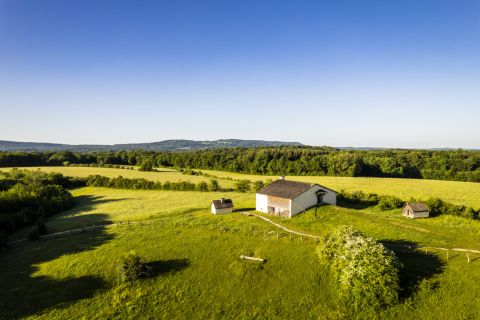 Prairie verte et ferme basse sous un ciel bleu, vue aérienne, salle Mission comté au Musée des Maisons Comtoises à Nancray