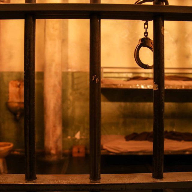 Cellule de prison avec barreaux noirs, menottes et décor souterrain chez LockedUp à Lieusaint