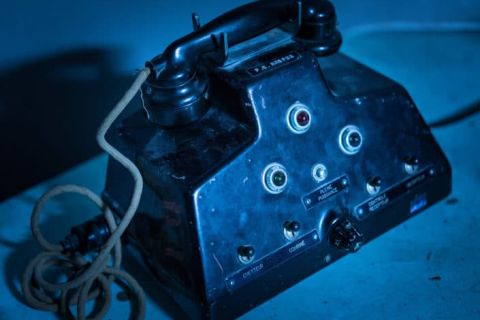 Poste de téléphone militaire noir à fils enroulés, éclairage bleu, salle Power Station chez Hydre Aventures à Lyon