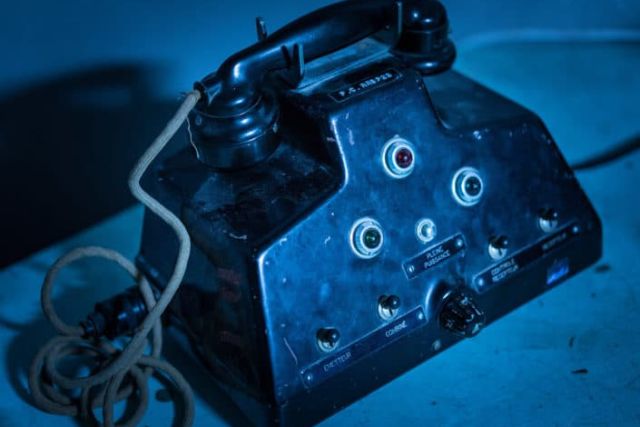 Poste de téléphone militaire noir à fils enroulés, éclairage bleu, salle Power Station chez Hydre Aventures à Lyon
