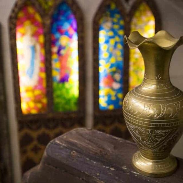 Décor gothique avec vitraux colorés, vase en laiton gravé et livre ancien dans la salle Crypte