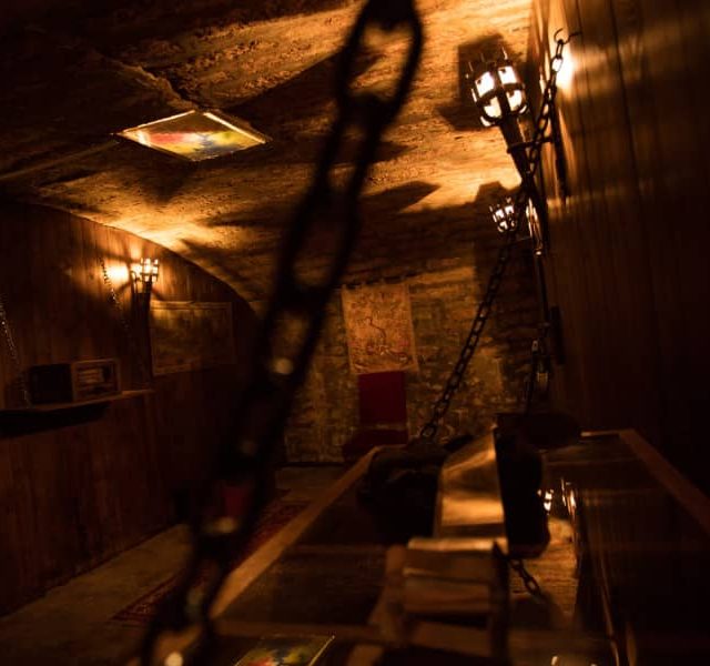 Corridor souterrain éclairé à la torche, chaînes et ambiance carcérale chez Skryptic Escape Game