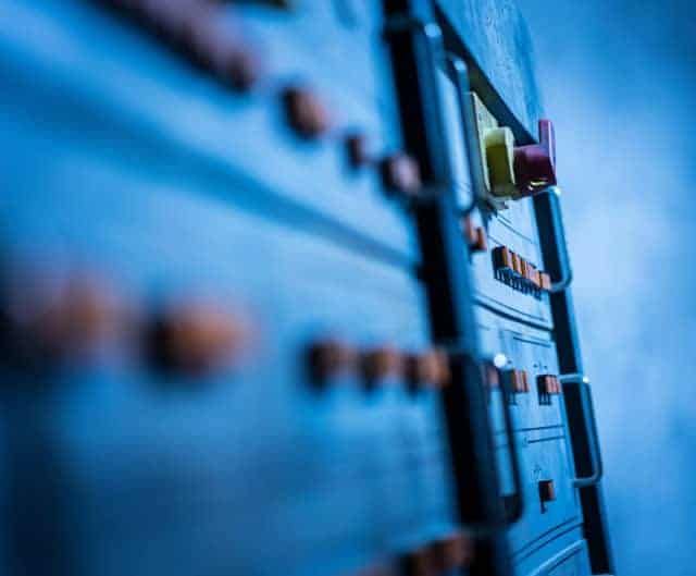 Panneau d'équipements bleu aux commutateurs en gros plan, salle PC Sécurité chez Hydre Aventures à Lyon