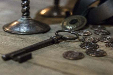 Grosse clé ancienne et pièces de monnaie sur un établi, salle Les mousquetaires chez Mystery Escape à Paris