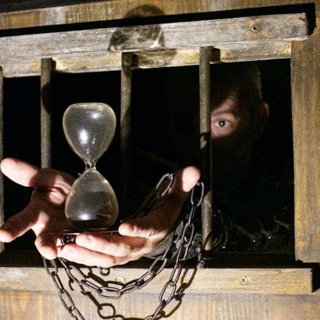 Prisonnier enchaîné tenant un sablier dans un cachot médiéval chez Escape Time Châteaudun