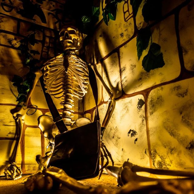 Squelette doré éclairé en jaune dans un décor de ruines antiques poussiéreuses