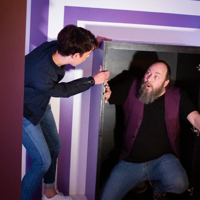 Joueur ouvrant la porte d'un coffre où surgit un homme barbu au gilet violet, salle La Grande Illusion, The Box Escape Games
