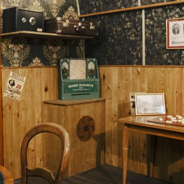 Petit bureau en bois, lampe à huile et cadres sur un mur lambrissé, salle Le Silver Express chez Escape Time à Pertuis