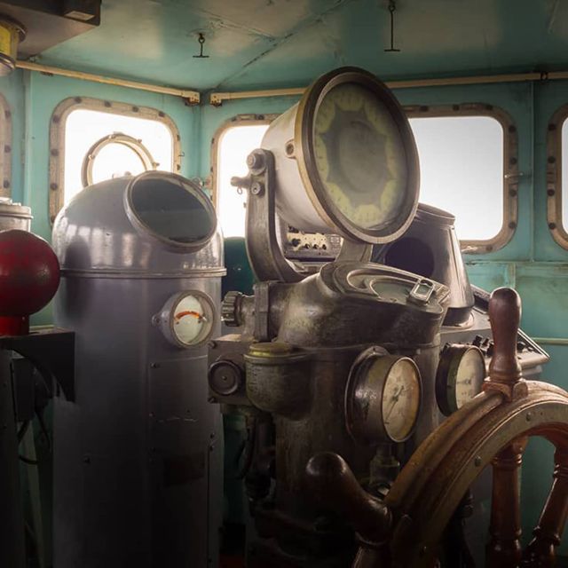 Poste de pilotage ancien avec barre à roue, projecteur et cuivres, salle Titanic chez Prisme Escape Game