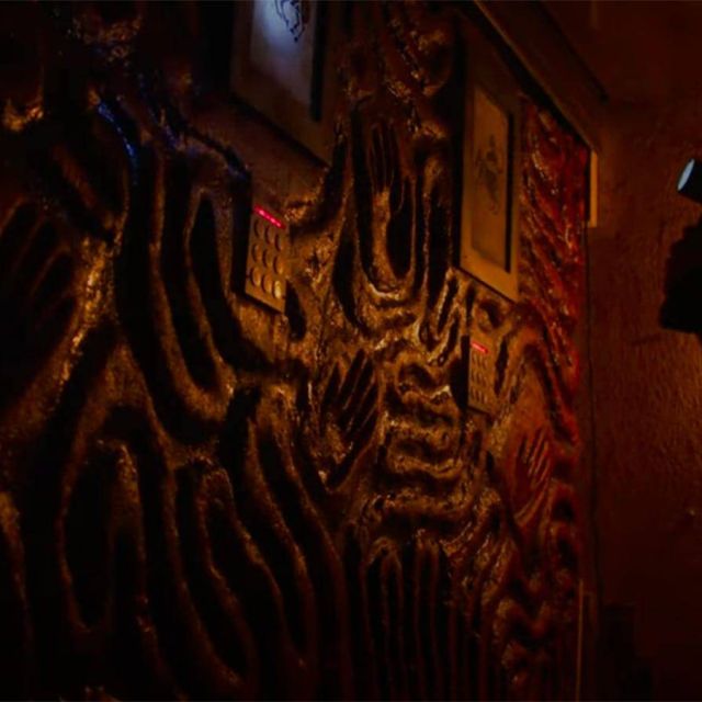 Mur sculpté de motifs sinueux dans une lumière ocre, silhouette au fond, salle La secte chez Freeing à Saint-Maximin