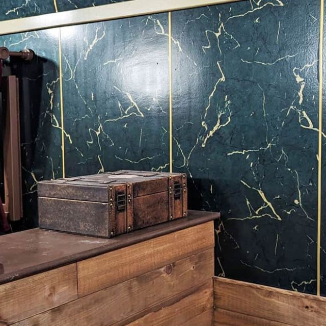 Meuble en bois, coffre et cadre ancien sur mur de faux marbre vert, salle Le Silver Express chez Escape Time à Angers