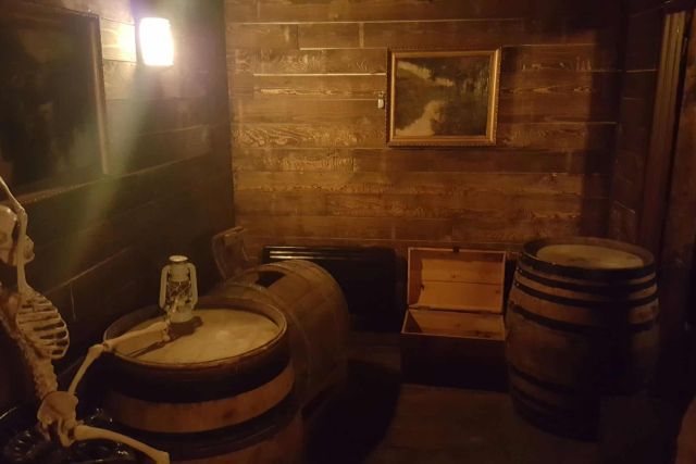 Cave de bois avec squelette, tonneaux et lanterne, salle Le globe des vents chez Escape Game Chalezeule