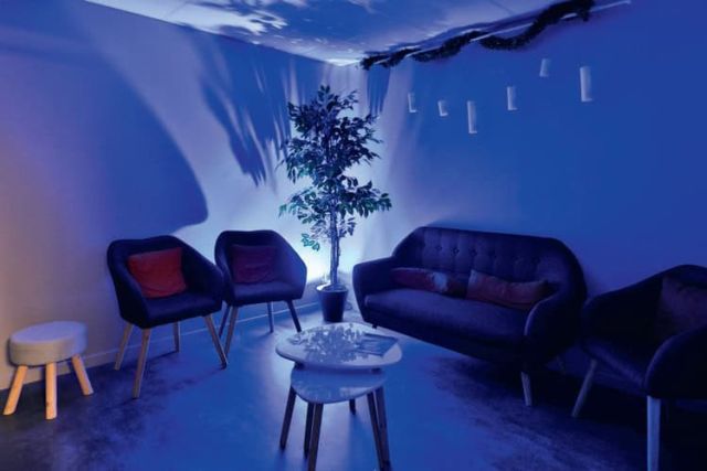 Salon d'attente baigné de lumière bleue, fauteuils et plante verte, chez Échap'Temps à Challans