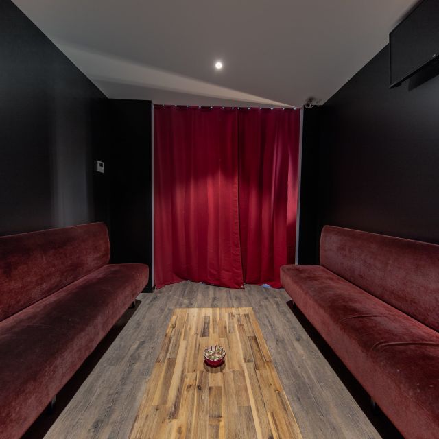 Longue salle noire à banquettes de velours rouge face à un rideau écarlate, Spirit Game à Douvaine