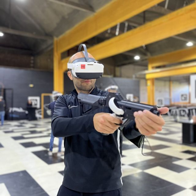 Joueur casqué de réalité virtuelle tenant une arme factice, sol à damier et poutres jaunes, Cube Challenges, Team Square