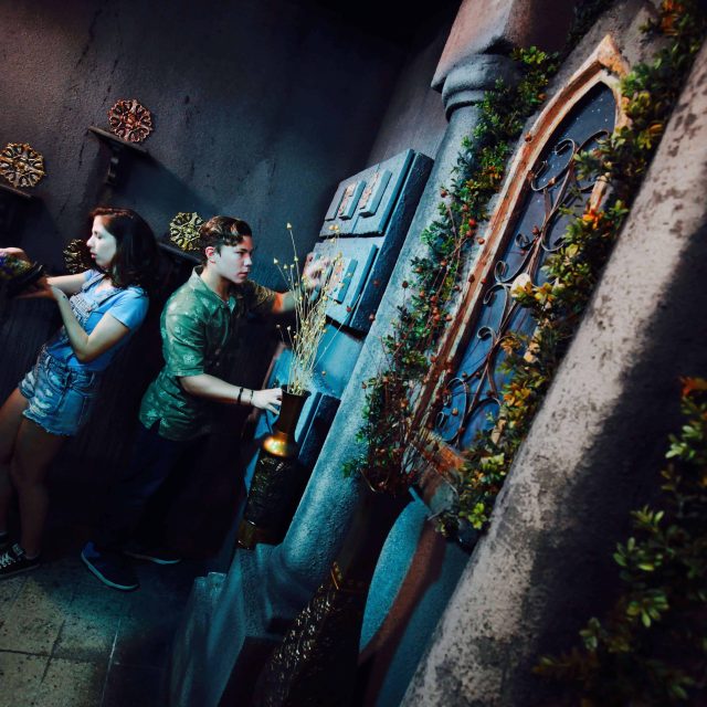 Deux joueurs explorent une ruelle bleue et dégradée, ornements dorés et végétation, chez Lockbusters Escape Game Orlando