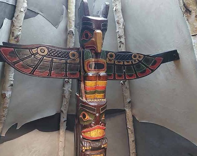 Totem sculpté et peint aux ailes rouges devant des troncs de bouleau, salle La ruée vers l'or chez Time Lapse