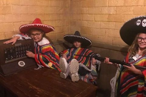 Trois enfants en ponchos et sombreros à têtes de mort autour d'un vieux poste, salle Les Bandidos des bonbons, TooLate Tours