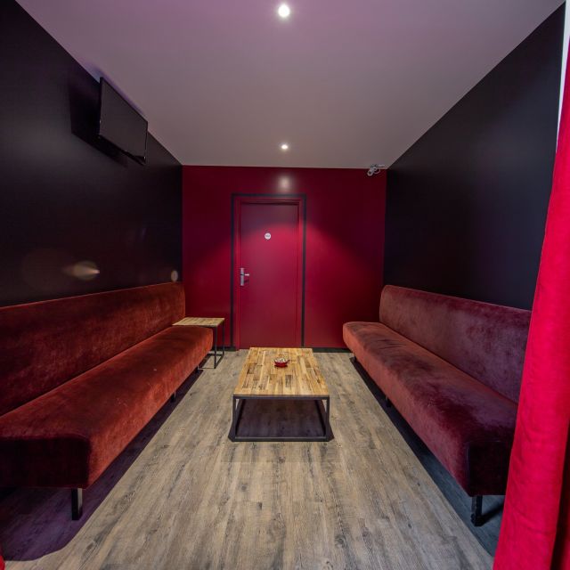 Salle d'attente aux banquettes bordeaux et rideaux rouges autour d'une table basse, Spirit Game à Douvaine