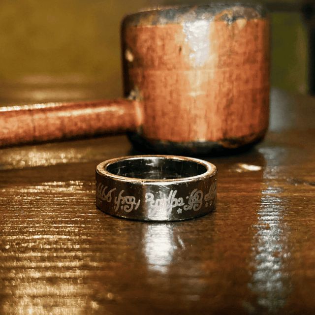 Bague gravée posée sur une table en bois devant une louche en cuivre, salle Le pouvoir de l'anneau