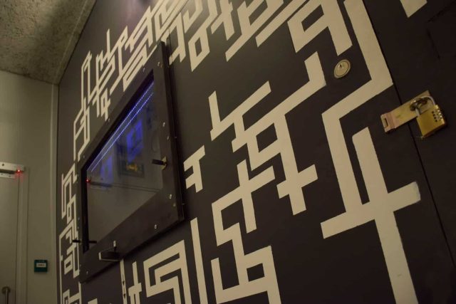 Mur noir couvert de motifs de labyrinthe blancs et grand écran, salle Police Academy de Palamento City chez Happy Hour à Paris