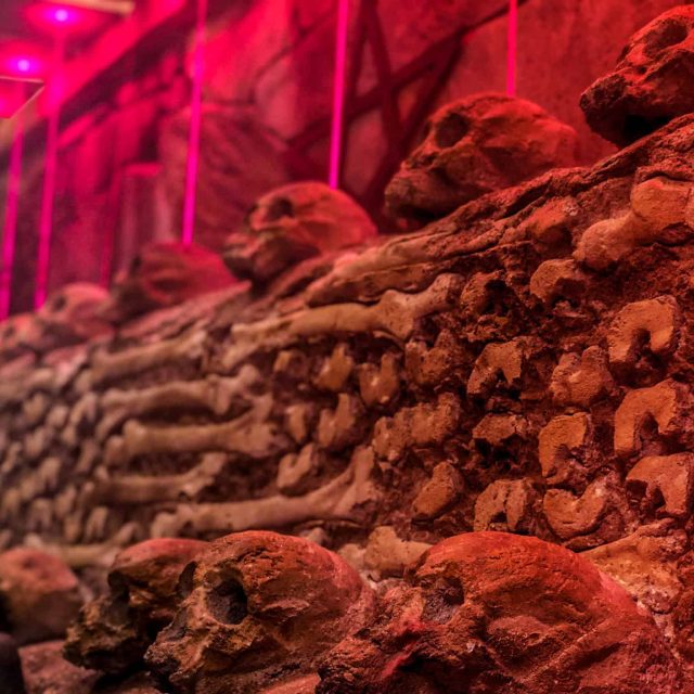 Décor souterrain en terre et pierres rouges éclairé par des néons roses dans Mystère à Lived Street