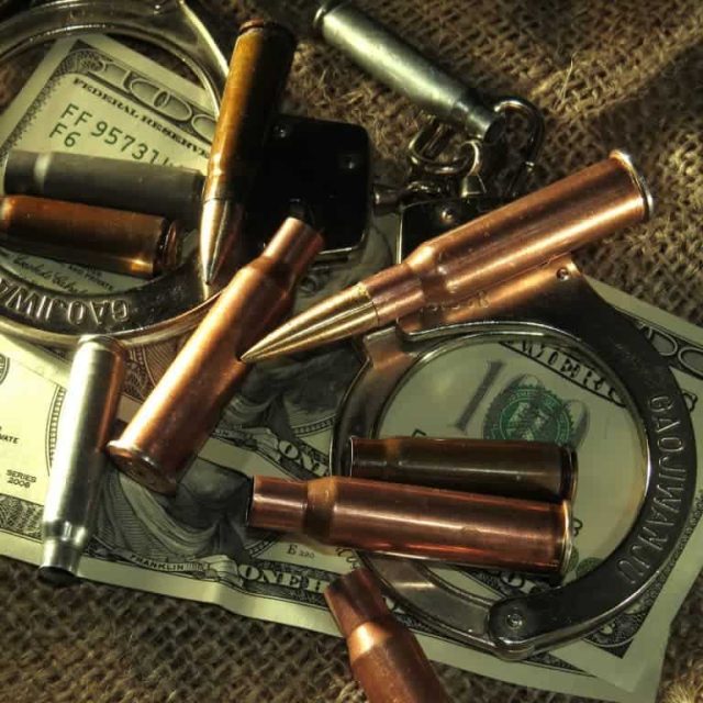 Gros plan de balles de cuivre, menottes et dollars posés sur un sac, salle Infiltrés chez Escape Game Poitiers