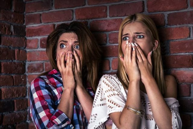 Deux jeunes femmes effrayées, mains sur la bouche, devant un mur de brique, salle Où est Jessy chez Crazy Rooms